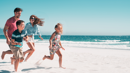 mom and dad running on white sand beach with their young son and daughter. on a bright baby blue sky day all smiling 